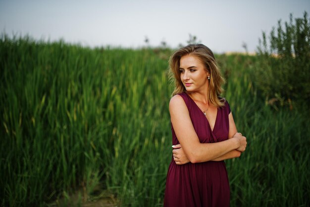 Blonde sensual woman in red marsala dress posing in the reeds