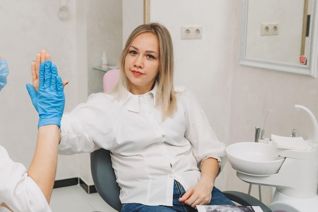 The blonde sits in a chair in the dentist's office and touches the doctor's hand to compromise that she will definitely recover after the treatment process.