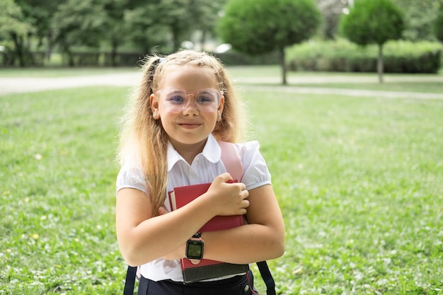 blonde smiling schoolgirl in school uniform holding notebook with pink backpack back to school