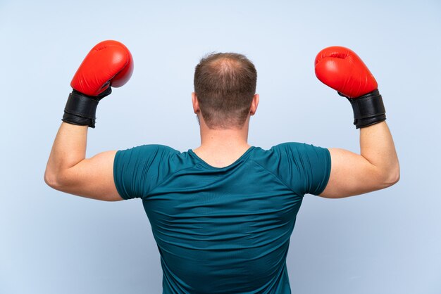 Blonde sport man over blue wall with boxing gloves