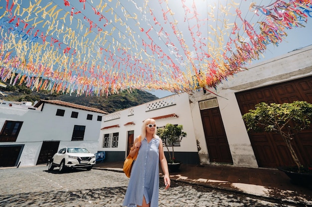 A blonde in a sundress with a backpack walks along the street of the Old town of Garachico on the island of TenerifeSpain Canary Islands