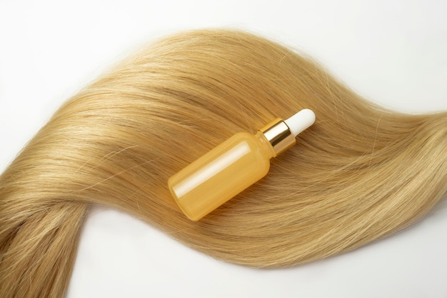 A blonde tress with a natural oil or serum for hair care lying on it