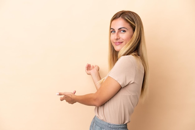 Blonde Uruguayan girl isolated on beige background extending hands to the side for inviting to come