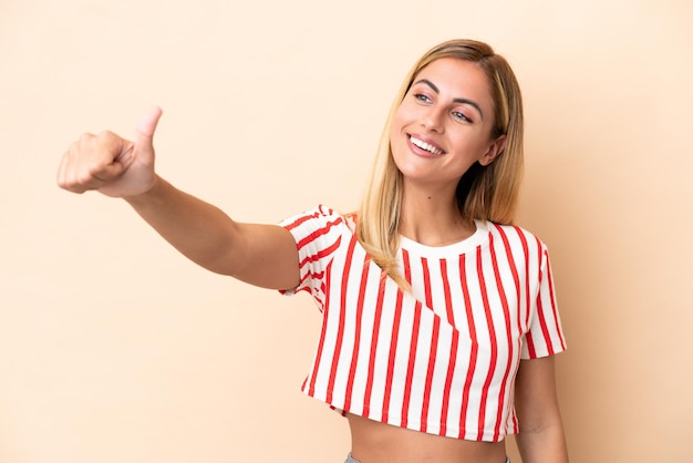 Blonde Uruguayan girl isolated on beige background giving a thumbs up gesture