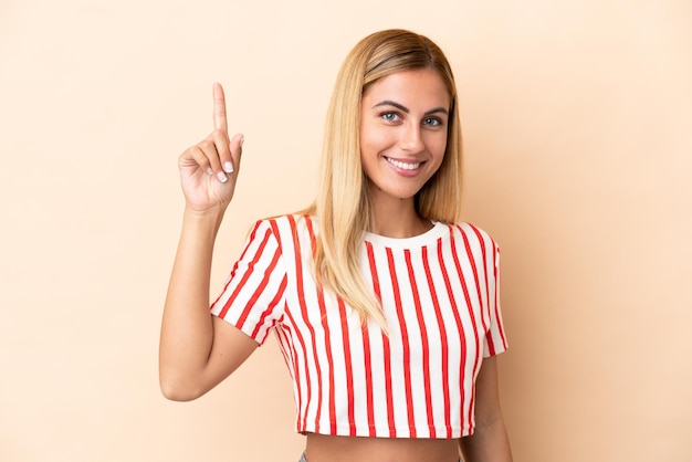 Blonde Uruguayan girl isolated on beige background pointing up a great idea