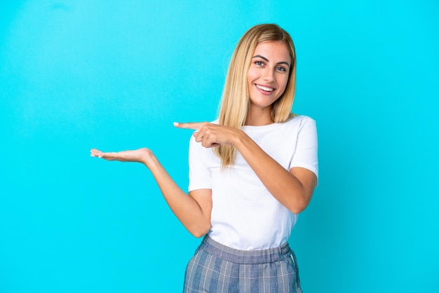 Blonde Uruguayan girl isolated on blue background holding copyspace imaginary on the palm to insert an ad