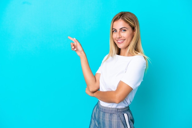 Blonde Uruguayan girl isolated on blue background pointing finger to the side