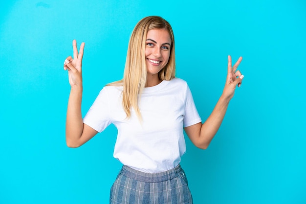 Blonde Uruguayan girl isolated on blue background showing victory sign with both hands