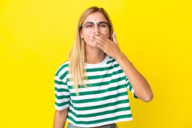 Blonde Uruguayan girl isolated on yellow background happy and smiling covering mouth with hand