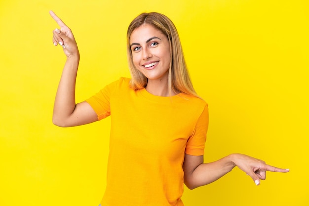 Blonde Uruguayan girl isolated on yellow background pointing finger to the laterals and happy