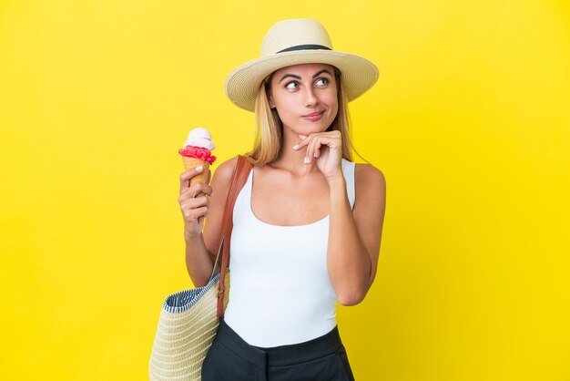 Blonde Uruguayan girl in summertime holding ice cream isolated on yellow background having doubts and thinking