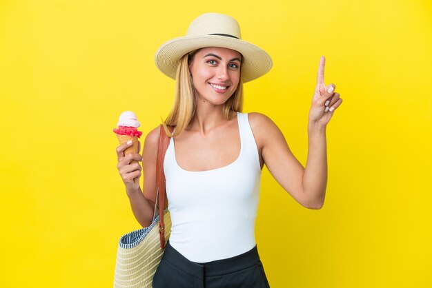 Blonde Uruguayan girl in summertime holding ice cream isolated on yellow background pointing up a great idea