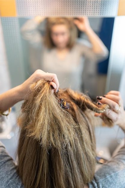 Blonde and white woman in front of the mirror and fixing her hair to comb and brush it