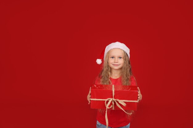 blonde with blue eyes in a red Tshirt in a Santa Claus hat holding a gift box