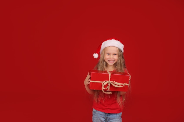 blonde with blue eyes in a red Tshirt in a Santa Claus hat holding a gift box