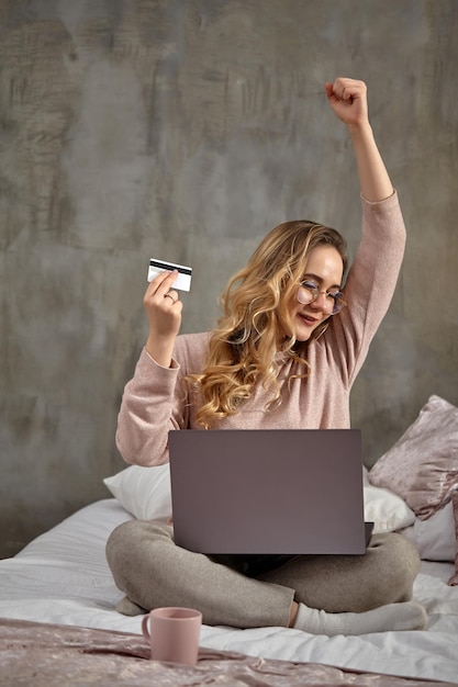 Blonde woman blogger in glasses casual clothing smiling raised her fist holding white plastic card s...