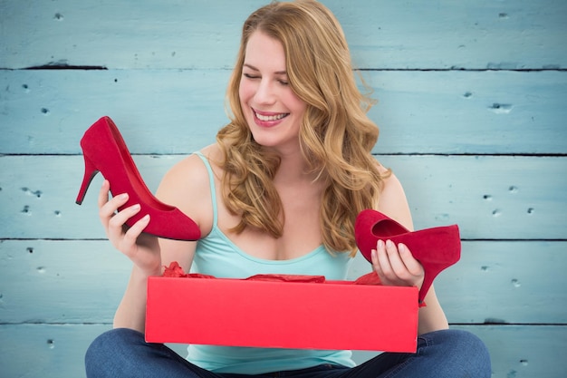 Blonde woman discovering shoes in a gift box against painted blue wooden planks