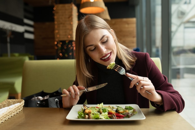 Blonde woman eating green healthy tasty eco salad on city cafe