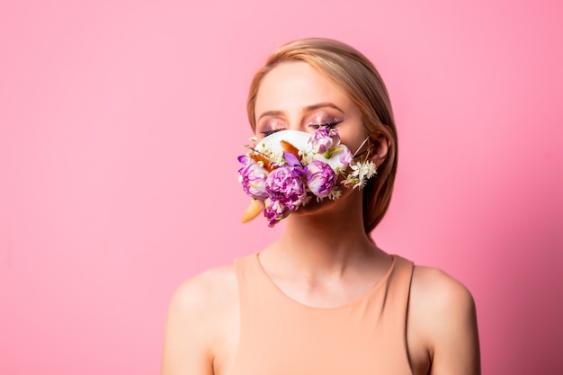 Photo blonde woman in face mask with flowers on pink background