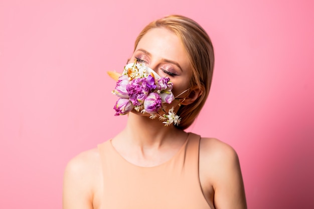 Photo blonde woman in face mask with flowers on pink background