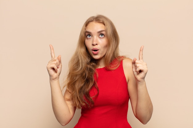 Blonde woman feeling awed and open mouthed pointing upwards with a shocked and surprised look