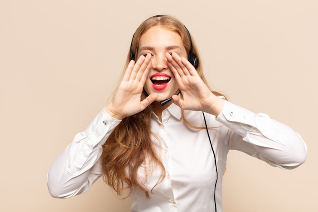 Blonde woman feeling happy, excited and positive, giving a big shout out with hands next to mouth, calling out