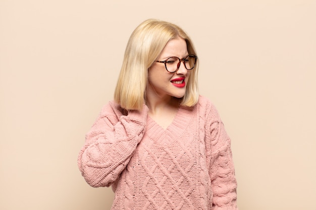 Blonde woman feeling stressed, frustrated and tired, rubbing painful neck, with a worried, troubled look