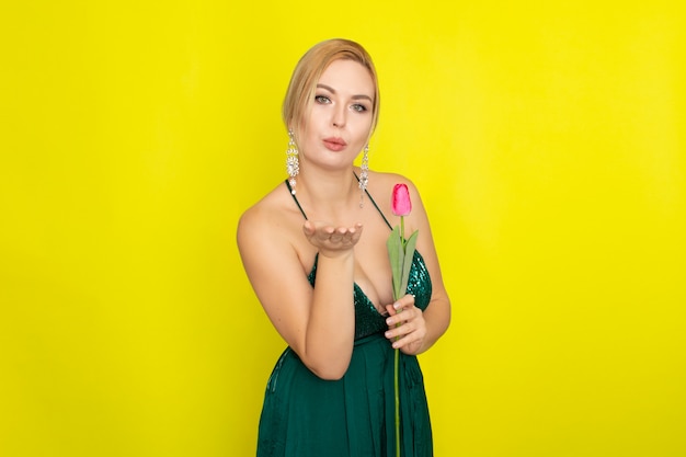 Blonde woman in green dress holding one pink tulip