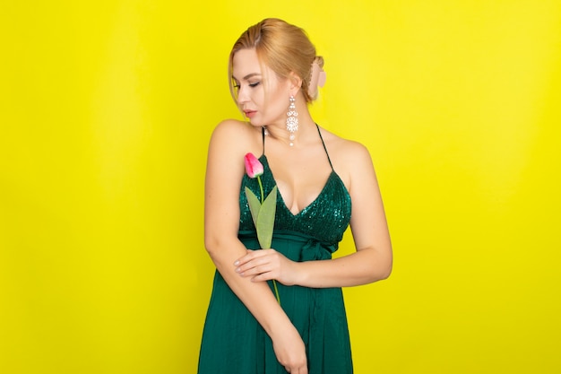 Blonde woman in green dress holding one pink tulip