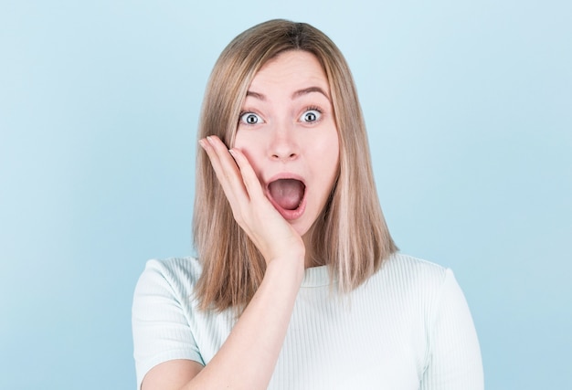 Blonde woman happy and surprised shouts holds cheek by hand .