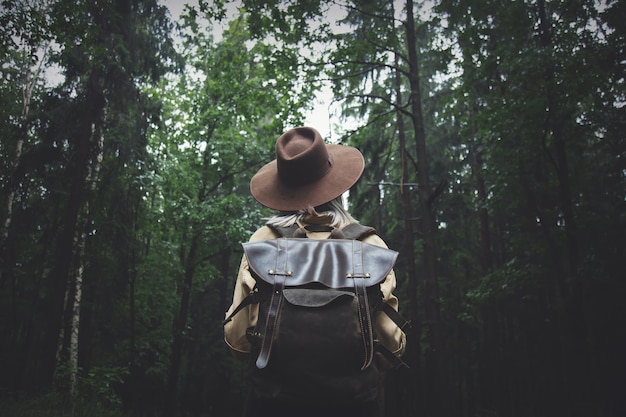 Blonde woman in hat with backpack in rainy day in forest