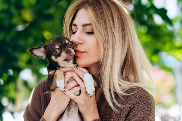 Blonde woman holding in her hands her pet and kissing it. - Image