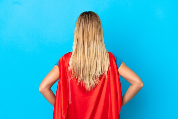 Blonde woman over isolated background in superhero costume in back position