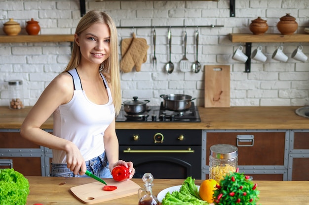 Blonde woman in the kitchen cuts red pepper on salad