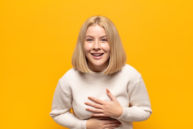 Blonde woman laughing out loud at some hilarious joke, feeling happy and cheerful, having fun