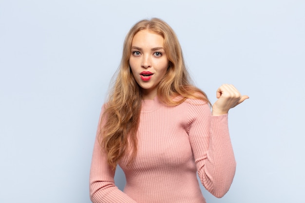 Blonde woman looking astonished in disbelief, pointing at object on the side and saying wow, unbelievable