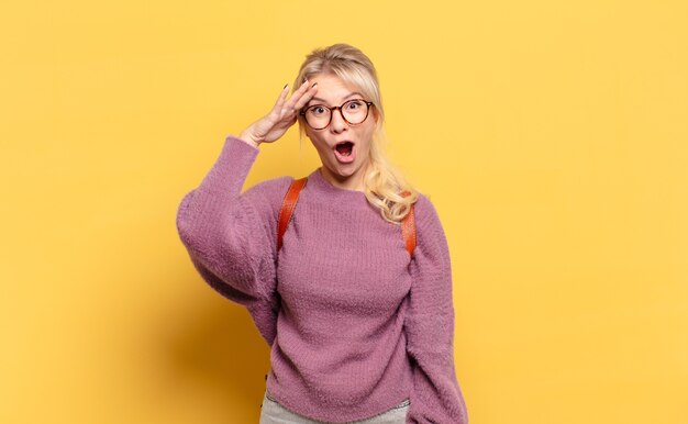 Blonde woman looking happy, astonished and surprised, smiling and realizing amazing and incredible good news