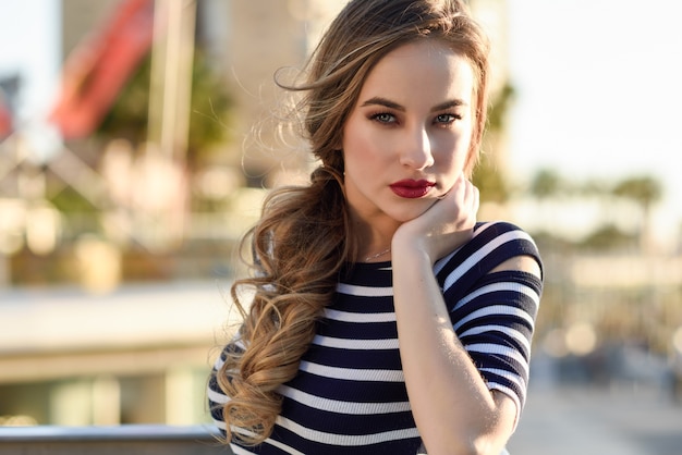 Blonde woman, model of fashion, sitting in urban background.