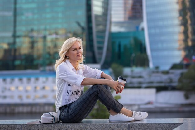 Blonde woman resting with a cup of coffee on the background of skyscrapers