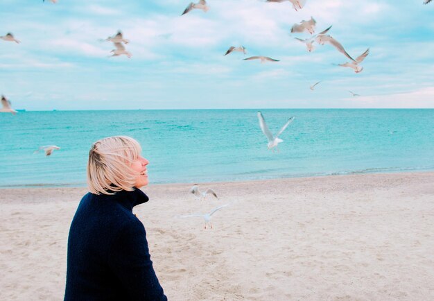 blonde woman and seagulls in cloudy day on the sea coast