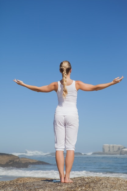 Blonde woman standing on beach on rock