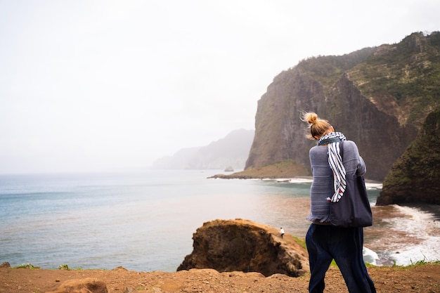 Blonde woman taking photos with a digital camera of the sea from a cliff