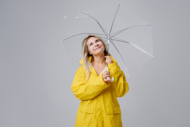 Photo blonde woman wearing yellow raincoat holding transparent umbrella checking weather if it is raining