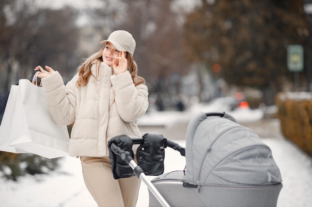 Blonde woman with baby stroller walking in the city with shopping packages