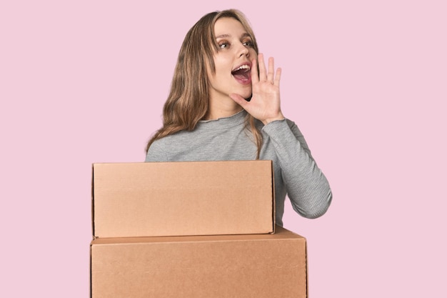 Blonde woman with cardboard boxes moving shouting and holding palm near opened mouth