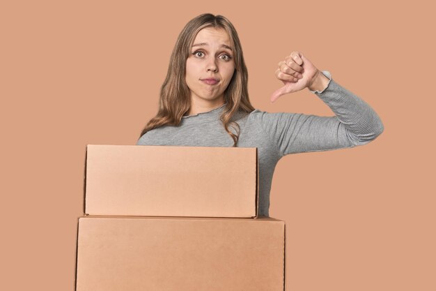 Blonde woman with cardboard boxes moving showing a dislike gesture thumbs down Disagreement concept