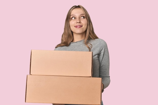 Photo blonde woman with cardboard boxes moving on studio backdrop dreaming of achieving goals and purposes