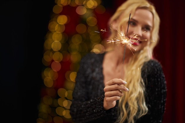 Blonde woman with long curly hair standing looking aside holding sparkles smiling