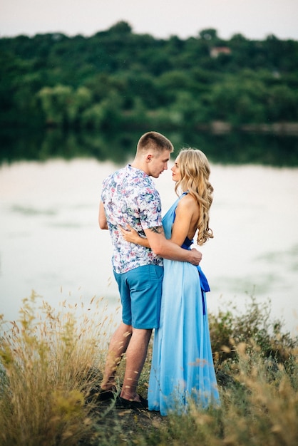 Blonde woman with loose hair in a light blue dress and a guy in the light of sunset in nature