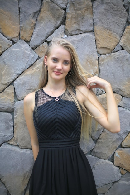 Blonde young woman against stone wall background smiling and posing on background of vineyards